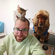 Jocker participe au concours pour gagner de l'argent avec cette photo : man, cat, dog, pet, selfie, portrait, indoors, hoodie, glasses, beard, curly_hair, calico_cat, brown_dog, sitting, animal, companion, funny, home, furniture, wheelchair