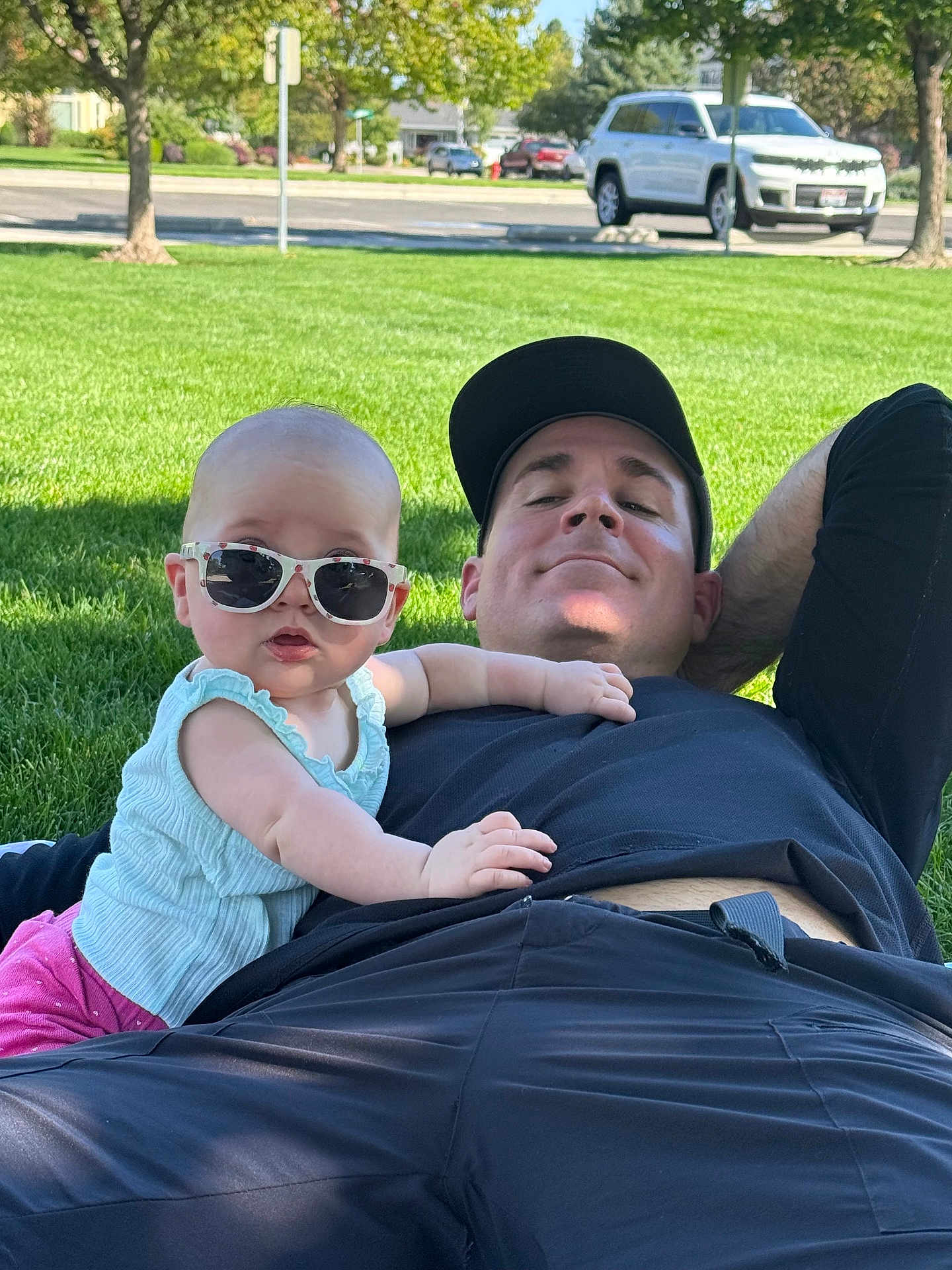 Lucy is registered to the contest to win money with this photo: baby, sunglasses, man, grass, park, outdoor, relaxing, casual, child, person, summer, greenery, shade, clothing, cap, resting, sunny, pink_pants, blue_top, smiling