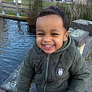 Karim participe au concours pour gagner de l'argent avec cette photo : toddler, child, smile, jacket, outdoor, water, canal, stone, hand, face, happy, winter_clothing, nature, park, fence, trees, urban, daylight, person, cute