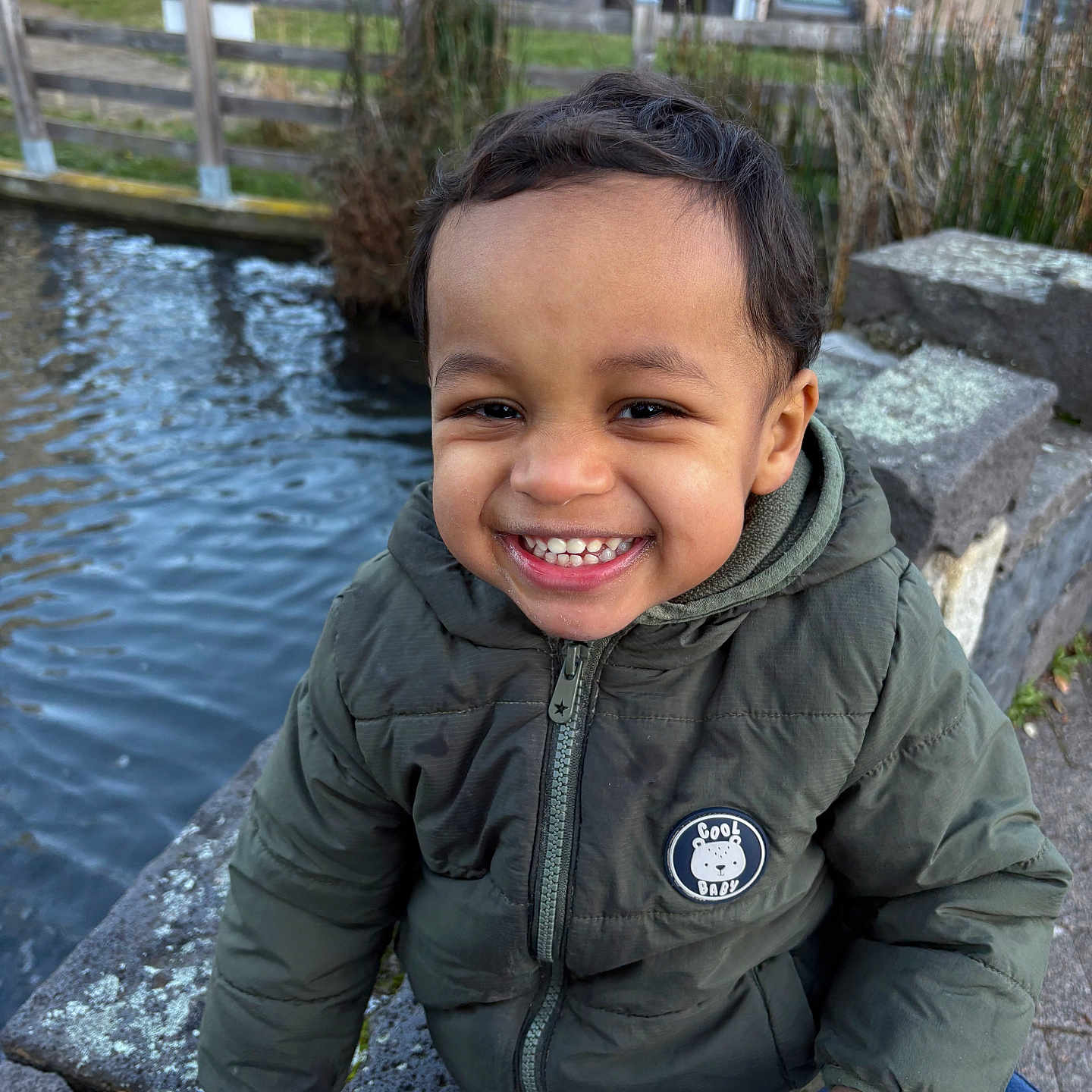 Karim participe au concours pour gagner de l'argent avec cette photo : canal, child, cute, daylight, face, fence, hand, happy, jacket, nature, outdoor, park, person, smile, stone, toddler, trees, urban, water, winter_clothing