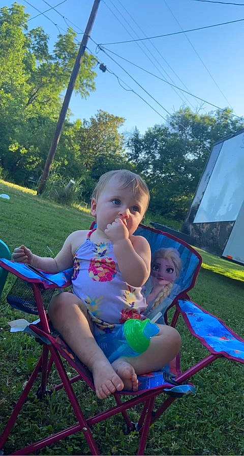 Addison is registered to the contest to win money with this photo: chair, child, electric_blue, event, folding_chair, fun, grass, lap, leisure, outdoor_furniture, person, plant, recreation, shade, shorts, sitting, sky, summer, tent, toddler