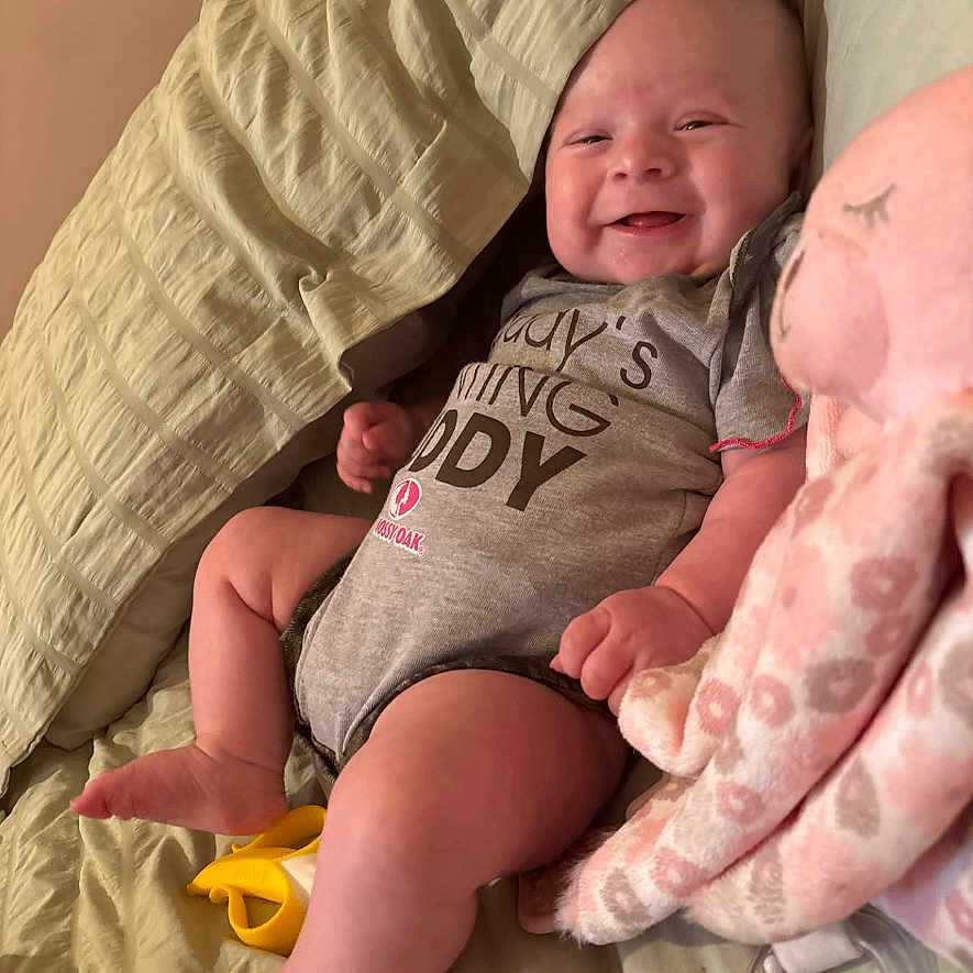 Erin joined the competition — help win amazing prizes! baby, banana_toy, bed, blanket, child, cute, face, foot, hand, happy, indoor, infant, lying_down, octopus_toy, onesie, person, plush_toy, skin, smile, young