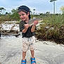 child, boy, fish, beach, sand, grass, nature, outdoor, cloudy_sky, cap, shorts, sandals, happy, catch, fishing, water, shore, smile, summer, vacation