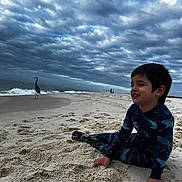 Levi joined the competition — help win amazing prizes! child, beach, sand, cloudy_sky, bird, ocean, water, smiling, sitting, outdoor, nature, waves, shoreline, dark_hair, long_sleeves, patterned_clothing, playful, relaxed, daytime, coastal