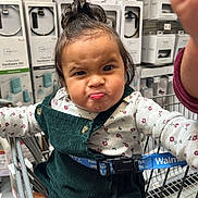 Kylee joined the competition — help win amazing prizes! toddler, child, shopping_cart, store, hardware, baby, clothing, green_overall, floral_shirt, face, expression, person, indoor, cute, hair, hand, seatbelt, retail, aisle, curly_hair
