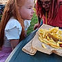 child, girl, woman, food, french_fries, table, outdoor, park, grass, trees, people, glasses, red_hair, white_clothing, pink_clothing, daylight, tent, event, nature, portrait
