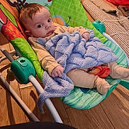 Antoni is registered to the contest to win money with this photo: baby, infant, blanket, baby_rocker, jungle_animals, monkey, tiger, wooden_floor, pajamas, knitted_blanket, indoor, child, face, hand, footwear, toy, furniture, colorful, relaxing, home