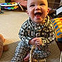 baby, child, smiling, pajamas, toy, wooden_toy, carpet, indoor, happy, sitting, patterned_clothing, cute, infant, playtime, floor, homedecor, colorful, furniture, hand, face