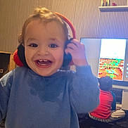 Oussaid a rejoint le concours — aidez-le/la à gagner de superbes lots ! blue_sweater, carpet, child, cute, family, furniture, happy, headphones, home, indoor, living_room, person, playing, red_shirt, screen, smile, striped_pants, technology, television, toddler