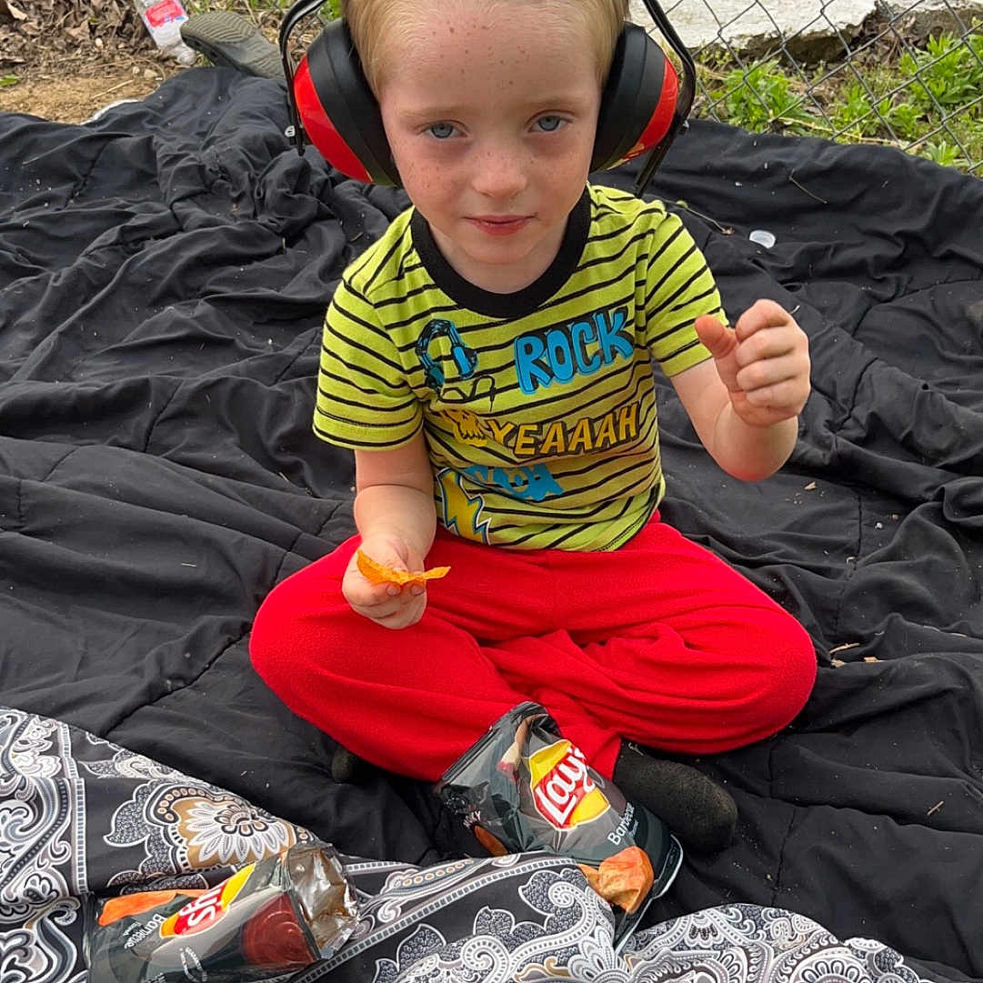 Brycen is registered to the contest to win money with this photo: baby, bodypart, clothing, electronics, face, finger, footwear, grass, hand, head, headphones, pants, person, photography, plant, portrait, shoe, shorts, soil, t_shirt