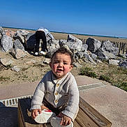 Haroun a rejoint le concours — aidez-le/la à gagner de superbes lots ! toddler, child, outdoor, beach, rocks, wooden_crate, sweater, sneakers, sky, grass, sand, person, nature, daylight, play, climbing, coast, casual_clothing, happy, cute