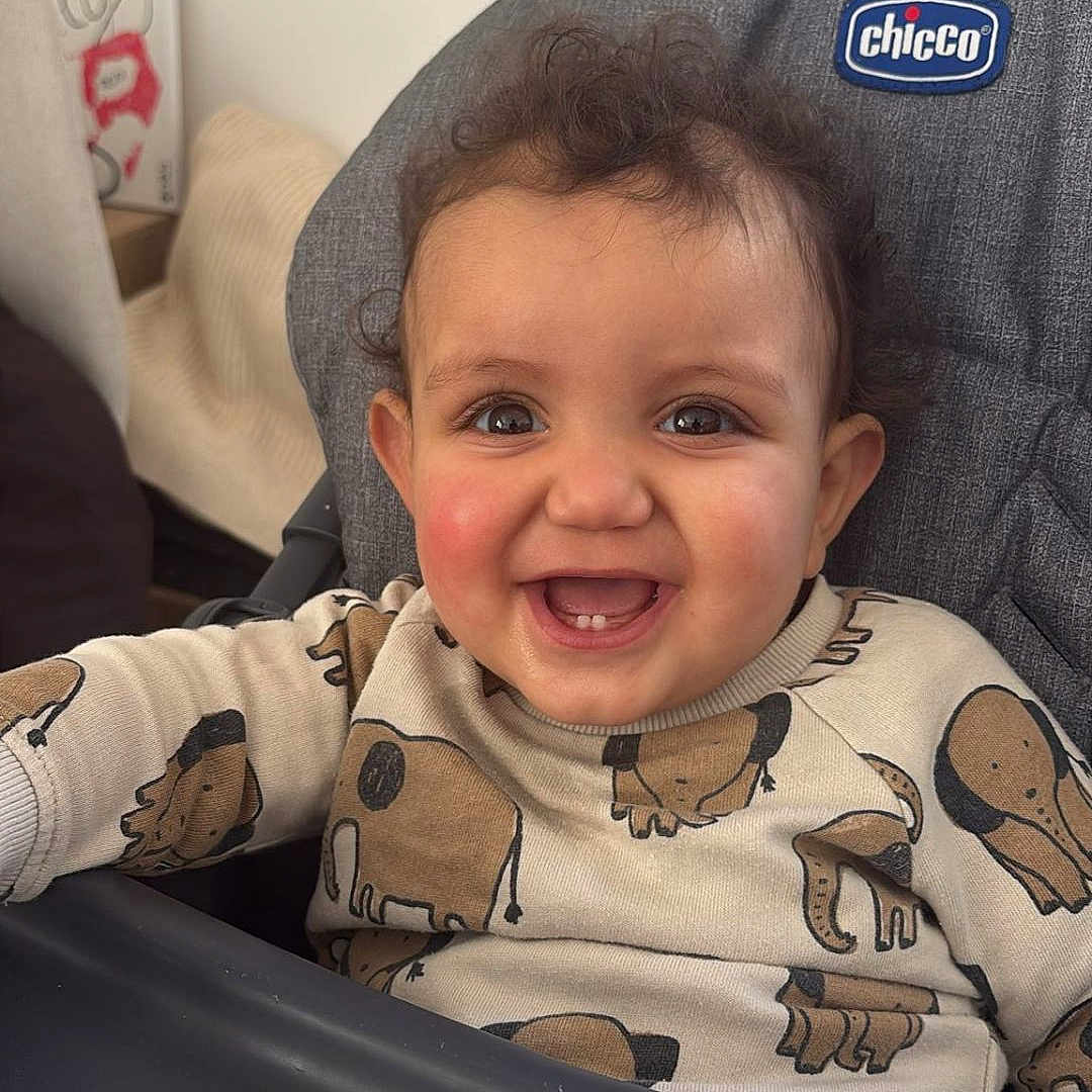 Haroun participe au concours pour gagner de l'argent avec cette photo : baby, child, high_chair, smile, curly_hair, sweater, animal_print, indoor, happy, face, person, cute, young_child, seated, expression, clothing, cheerful, infant, portrait, cozy