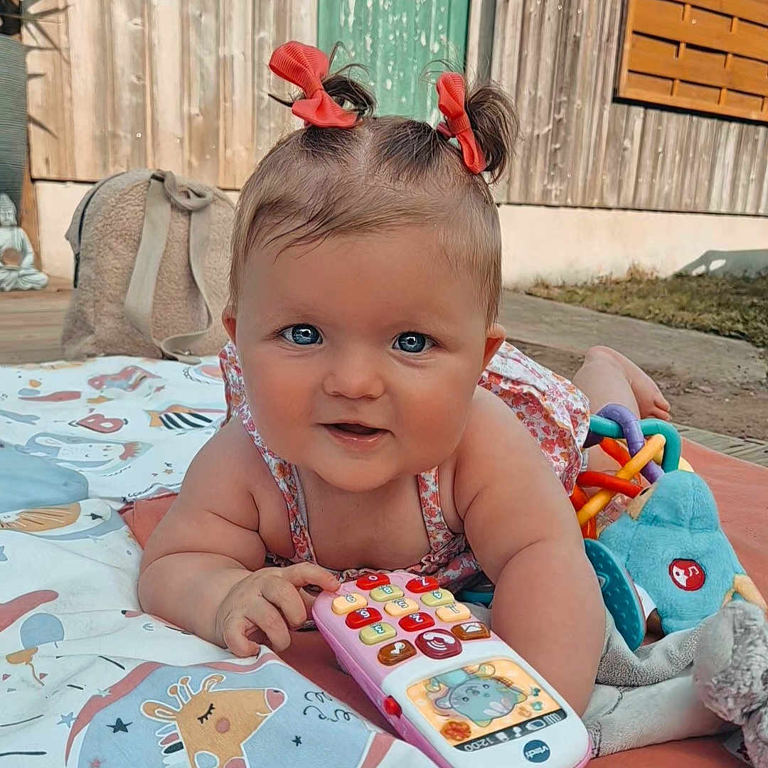 Aisyah participe au concours pour gagner de l'argent avec cette photo : baby, bows, child, colorful, curious, cute, face, grass, hands, infant, outdoor, pigtails, play_mat, portrait, smiling, soft_toys, toddler, toy_phone, wooden_wall, young_child