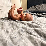 Raheem is registered to the contest to win money with this photo: baby, infant, bed, blanket, pacifier, hand, foot, cozy, indoor, child, cute, sleeping_area, pillow, furniture, skin, head, expression, relaxing, person, lying_down