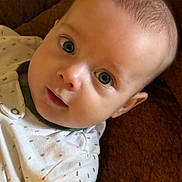 Micah joined the competition — help win amazing prizes! baby, infant, face, blue_eyes, clothing, white_outfit, patterned_clothing, blanket, brown_blanket, soft_texture, closeup, portrait, cute, child, young, skin, head, expression, person, indoors