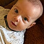 baby, infant, face, blue_eyes, clothing, white_outfit, patterned_clothing, blanket, brown_blanket, soft_texture, closeup, portrait, cute, child, young, skin, head, expression, person, indoors