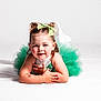 child, girl, tutu, green_bow, double_buns, temporary_tattoo, smiling, lying_down, studio_shot, white_background, sparkly_clothing, cute, happy, face, arms_crossed, young, portrait, playful, hair_buns, fashion