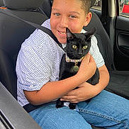 Thimble is registered to the contest to win money with this photo: animal, black_cat, boy, car_seat, casual_clothing, child, collar, cute, gas_station, holding, indoor, jeans, pet, portrait, seatbelt, short_hair, smiling, vehicle, window, yellow_eyes