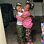 Legacy is registered to the contest to win money with this photo: child, hug, smile, girl, hair_bow, living_room, carpet, couch, shelf, plant, pants, boots, pink, white_shirt, camouflage_pants, happy, indoor, friendship, cute, playful