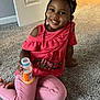 Legacy is registered to the contest to win money with this photo: child, girl, smile, bow, braids, pink_clothing, carpet, indoor, bottle, juice, happy, sitting, casual, home, portrait, cute, person, toddler, floor, relaxed