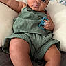 baby, child, infant, sunglasses, green_outfit, pacifier, cushion, indoor, portrait, cute, chubby, relaxed, fashion, accessory, skin, person, young_child, seated, looking_at_camera, casual