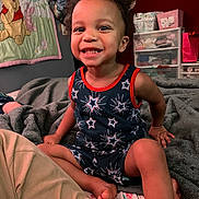 Kolton is registered to the contest to win money with this photo: toddler, child, smiling, indoor, bed, blanket, clothing, patterned_outfit, hair, face, person, furniture, storage, toy, quilt, winnie_the_pooh, happy, room, foot, casual