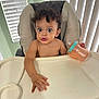 Arthur is registered to the contest to win money with this photo: toddler, child, high_chair, sippy_cup, curly_hair, wide_eyes, indoor, window_blinds, tray, hand, face, expression, skin, hair, person, seat, furniture, light, room, mouth