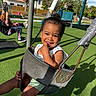 Jireh is registered to the contest to win money with this photo: toddler, child, swing, playground, smile, happy, outdoor, person, green_turf, sunlight, play_equipment, tree, shadow, casual_clothing, daytime, park, fun, recreation, summer, joy