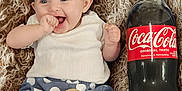 Meadow is registered to the contest to win money with this photo: baby, infant, smiling, red_headband, red_shoes, white_shirt, blue_shorts, polka_dots, textile, blanket, coca_cola_bottle, beverage, wooden_sign, three_months, happy, cute, sitting, portrait, indoor, person