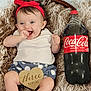 baby, infant, smiling, red_headband, red_shoes, white_shirt, blue_shorts, polka_dots, textile, blanket, coca_cola_bottle, beverage, wooden_sign, three_months, happy, cute, sitting, portrait, indoor, person