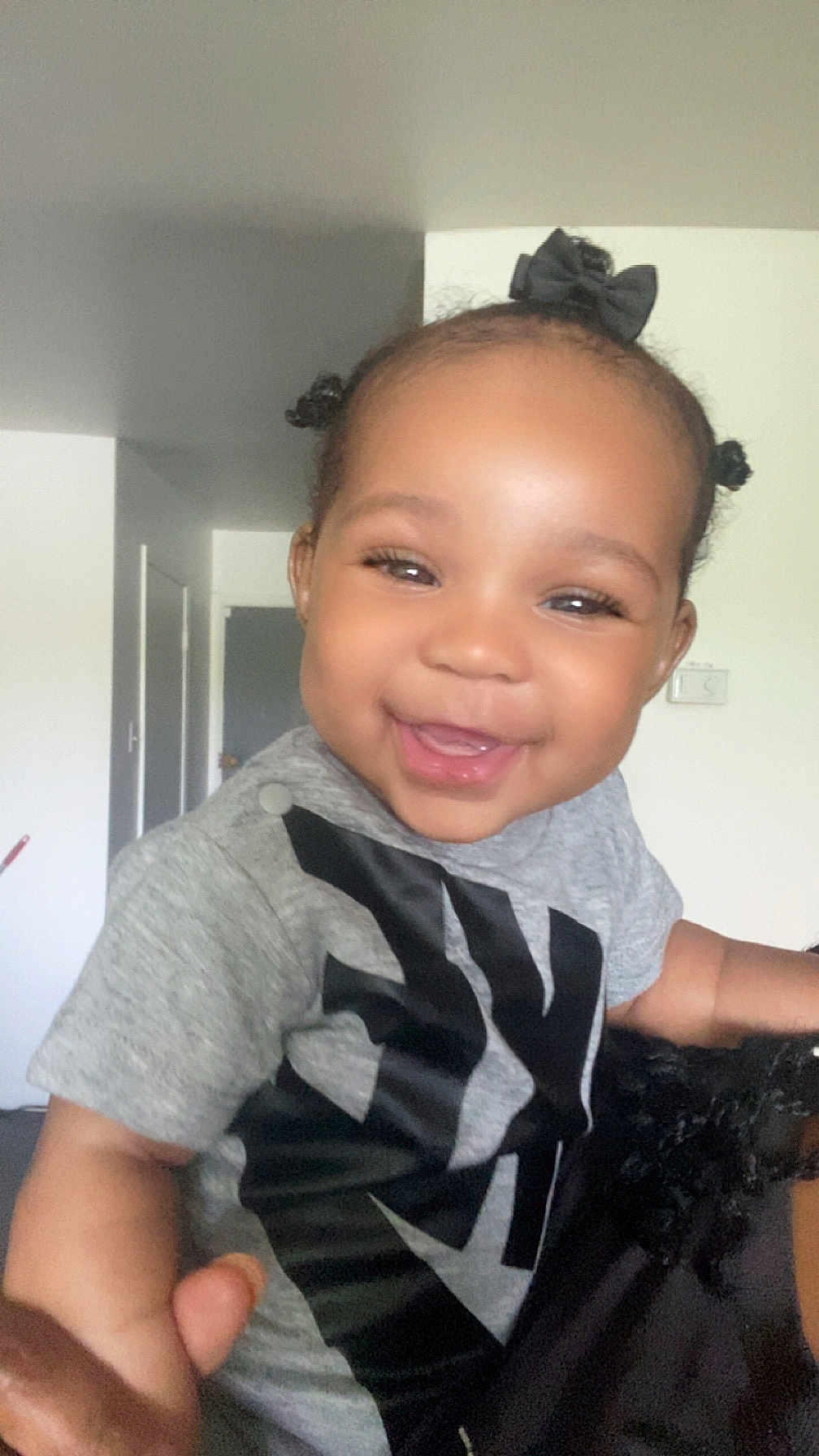 Brielle is registered to the contest to win money with this photo: toddler, child, smiling, happy, indoor, gray_shirt, hair_bows, baby, person, portrait, cute, black_hair, expression, young_child, joy, human, face, skin, casual_clothing, holding_hand