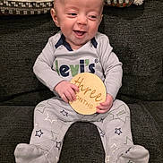 Silas is registered to the contest to win money with this photo: baby, blanket, child, clothing, couch, cute, fabric, face, happy, home, indoors, infant, levis, pajamas, pattern, person, sign, sitting, smiling, wooden_sign