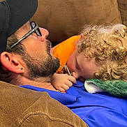 P.j joined the competition — help win amazing prizes! man, child, couch, curly_hair, glasses, cap, pacifier, blanket, orange_clothing, blue_clothing, brown_furniture, earring, facial_hair, resting, cuddling, indoor, close_up, comfort, nap, bonding