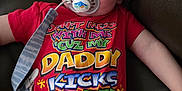 P.j is registered to the contest to win money with this photo: toddler, child, pacifier, red_shirt, curly_hair, sitting, couch, indoor, clothing, face, person, relaxed, cute, baby, infant, comfort, expression, colorful_text, strap, leisure