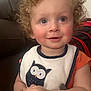 P.j is registered to the contest to win money with this photo: toddler, curly_hair, blue_eyes, bib, owl_design, orange_shirt, smiling, indoor, couch, child, person, young_child, cute, happy, portrait, face, hand, backpack, seated, casual