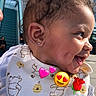 baby, child, smiling, side_profile, bib, outdoor, sunlight, curly_hair, earring, building, window, stairs, person, cute, dimples, happy, infant, wearing_clothes, daylight, emoji