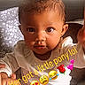Hazellbelle joined the competition — help win amazing prizes! baby, bed, child, curious, cute, face, floral_pattern, hair, hand_holding, head, indoors, infant, person, pillow, pony_tail, sitting, skin, smiling, text_overlay, white_pajamas