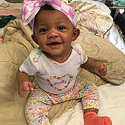 Hazellbelle joined the competition — help win amazing prizes! baby, child, smiling, sitting, bow, headband, pink, orange_socks, floral_pants, white_shirt, bed, pillows, blanket, indoors, cute, happy, portrait, infant, clothing, person