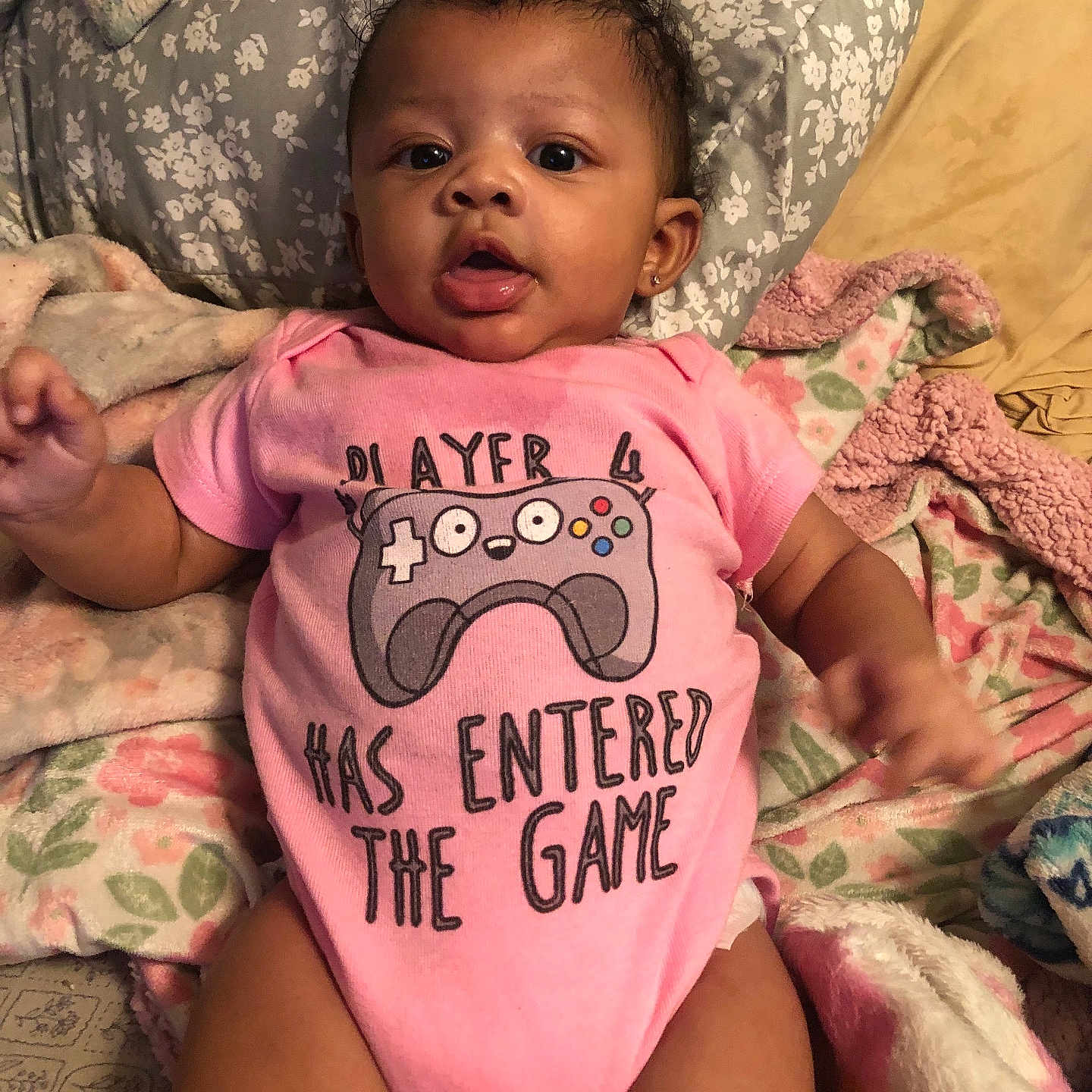 Hazellbelle joined the competition — help win amazing prizes! baby, bed, blanket, casual, child, comfort, cozy, cute, expression, face, floral_pattern, gaming_controller, indoors, infant, lying_down, pink_onesie, portrait, small_child, soft_texture, text_on_clothing