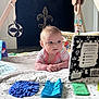 baby, infant, play_mat, high_contrast_book, wooden_baby_gym, hanging_toys, striped_clothing, floor, indoor, curious_expression, blue_eyes, fleur_de_lis, decor, soft_toys, child, person, early_learning, baby_playing, baby_toys, crawling