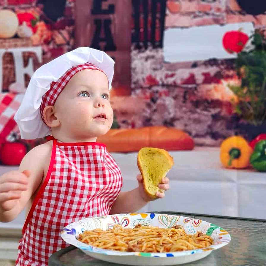 Louis joined the competition — help win amazing prizes! apron, baby, background, bread, chef_hat, child, cooking, cute, food, glass_table, indoors, kitchen_theme, plate, portrait, red_checkered, sitting, spaghetti, table, toddler, vegetables