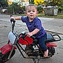 toddler, child, motorbike, barefoot, purple_shirt, outdoor, driveway, concrete, toy, handlebars, expression, backyard, trash_bin, fence, grass, trees, daylight, curious, small_vehicle, casual_clothing