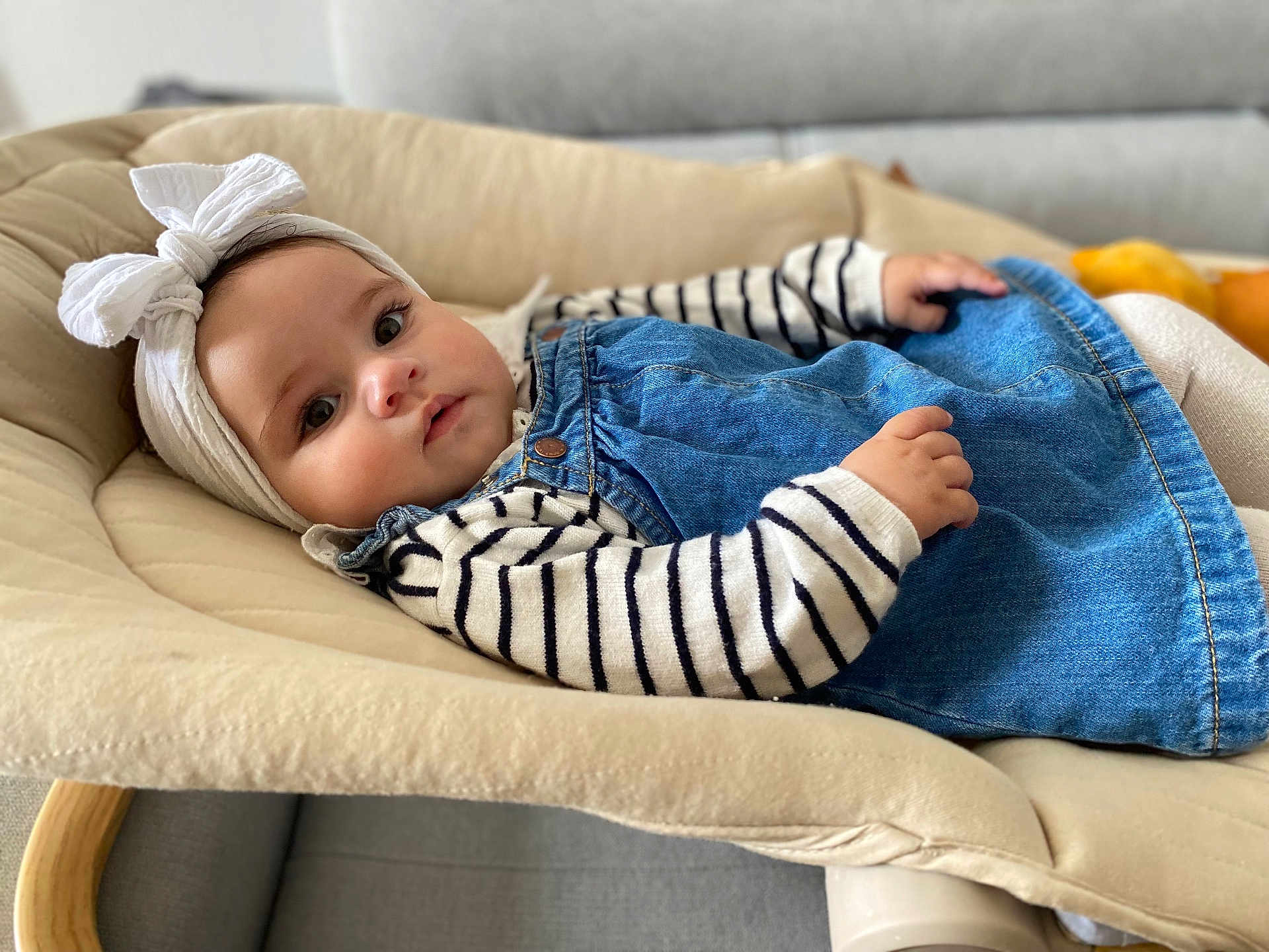 Ava participe au concours pour gagner de l'argent avec cette photo : baby, child, infant, girl, headband, bow, denim, dress, striped_shirt, cushion, chair, indoor, portrait, face, hand, soft_lighting, comfortable, cute, relaxed, young