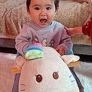 Henri participe au concours pour gagner de l'argent avec cette photo : blanket, carpet, child, clothing, cute, foot, furniture, hand, happy, home, indoor, person, play, plush_toy, rocking_toy, smile, sweater, toddler, toy, unicorn