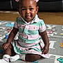 child, toddler, play_mat, girl, pink_bows, striped_dress, socks, smiling, tongue_out, indoors, carpet, cute, happy, sitting, young_child, person, floor_mat, playful, portrait, casual_wear