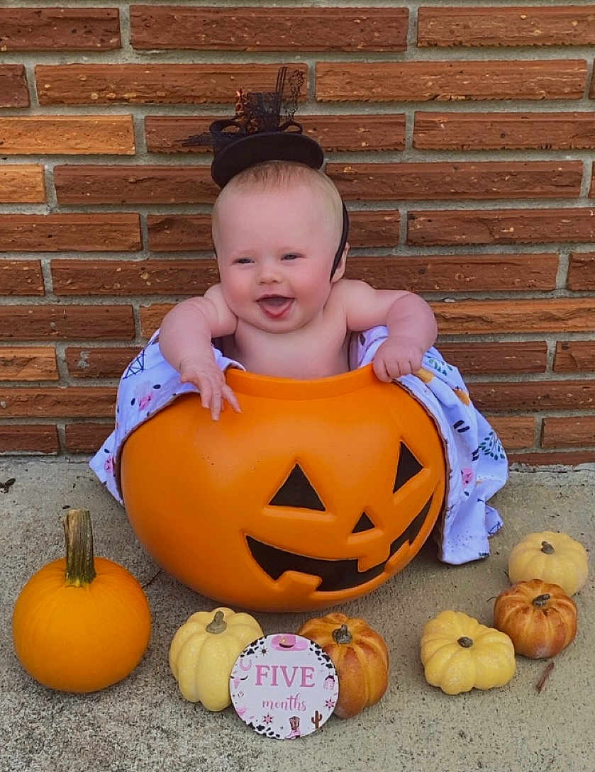 Nevaeh is registered to the contest to win money with this photo: baby, pumpkin, jack_o_lantern, brick_wall, concrete, hat, milestone_sign, smiling, cute, fall, autumn, holiday, festive, orange, yellow, small_pumpkins, child, costume, happy, outdoor