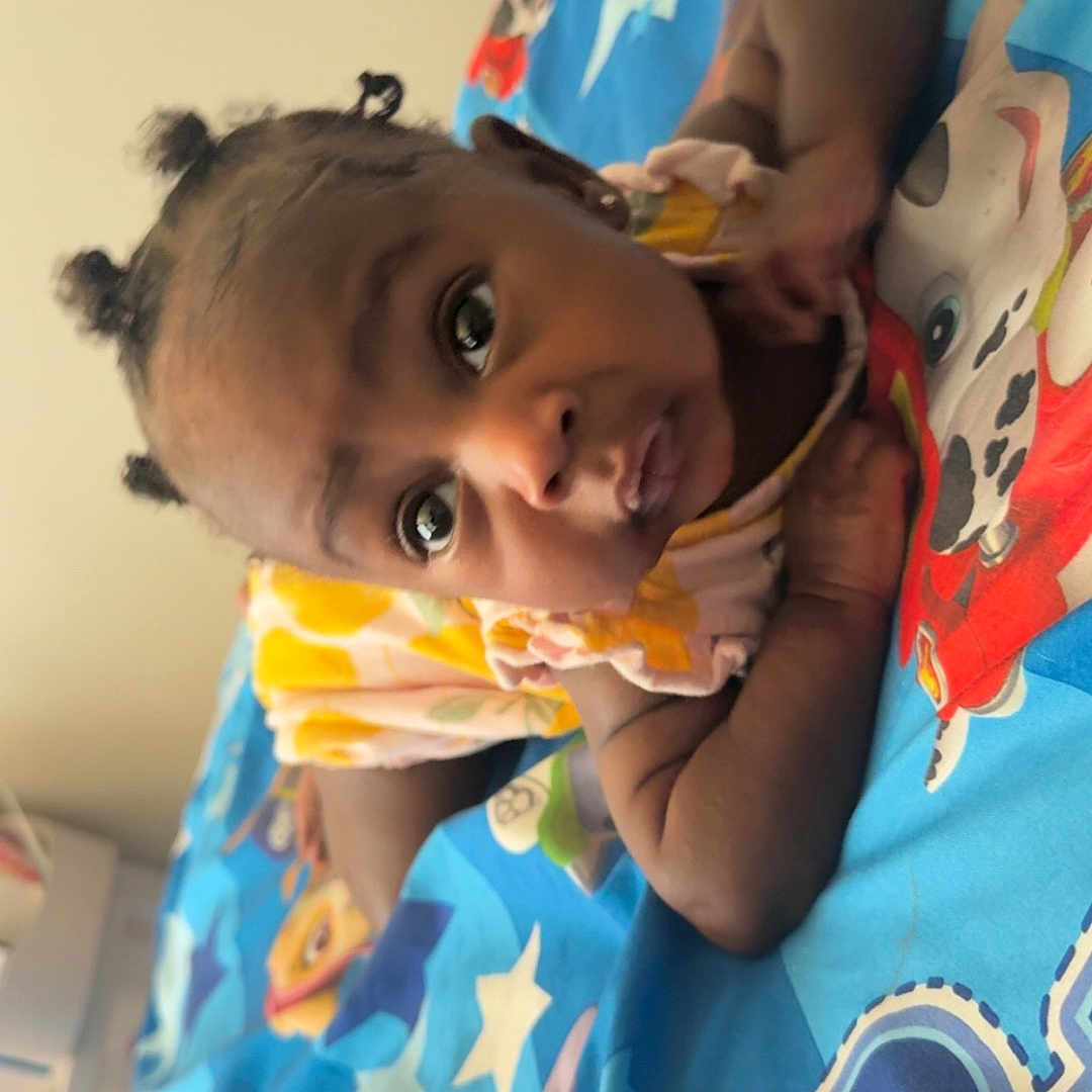 Janayah joined the competition — help win amazing prizes! baby, child, infant, cute, curious, indoor, blanket, colorful, cartoon, pajamas, lying_down, face, hair, eyes, skin, expression, soft_lighting, bedroom, comfort, person