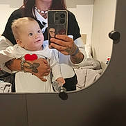 Tiago a rejoint le concours — aidez-le/la à gagner de superbes lots ! woman, baby, mirror, selfie, glasses, tattoo, bracelet, phone, bedroom, bed, blanket, white_clothing, heart, smile, holding, child, indoor, person, curious, reflection