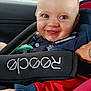 Tiago participe au concours pour gagner de l'argent avec cette photo : baby, child, car_seat, smiling, blue_jacket, red_pants, pacifier, face, person, indoors, seatbelt, happy, cute, infant, clothing, closeup, car_interior, safety, young, portrait