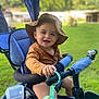 Djayden a rejoint le concours — aidez-le/la à gagner de superbes lots ! baby_clothes, blue_seat, cheerful, child, face, fun, green_grass, hand, happy, hat, nature, outdoor, person, playtime, smile, summer, sunlight, toddler, toy, tricycle